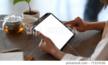 Cropped shot of young woman using digital tablet surfing internet while sitting in cafe. Cropped shot of young woman using digital tablet surfing internet while sitting in cafe. 75324586