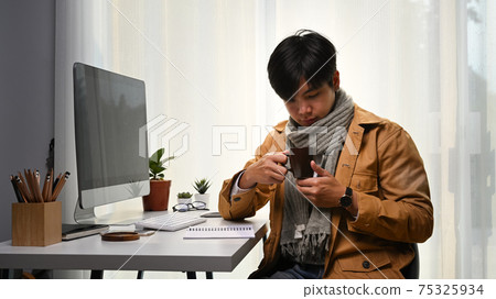 Handsome man holding a cup of coffee while sitting in front of computer at home office. Handsome man holding a cup of coffee while sitting in front of computer at home office. 75325934