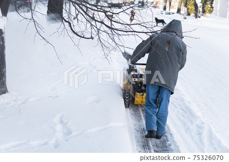 Man cleaning driveway with snow machines after a snow storm. Snow removal equipment working on the street. Cleaning of streets from snow. It's snowing. 75326070