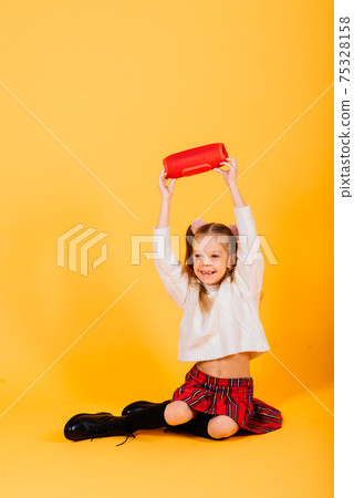 Young cute girl smiling and dancing with wireless portable speaker on yellow studio background. 75328158