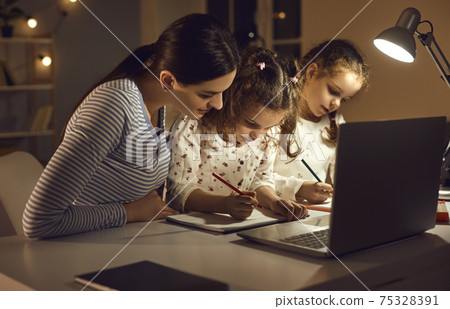 Concentrated children writing in copybooks sitting at desk with mom in the evening 75328391