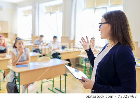 Portrait of talking middle-aged teacher woman in classroom with students 75328468