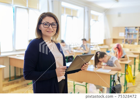 Portrait of mature woman teacher in classroom with digital tablet 75328472