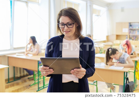 Portrait of mature woman teacher in classroom with digital tablet 75328475