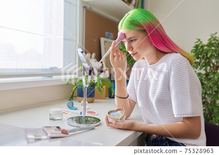Trendy, fashionable teenager girl with dyed colored hair doing makeup 75328963