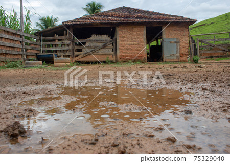 A kind of barn on a corral, after a heavy rain with the...A kind of barn on a corral, after a heavy rain with the ground full of puddles. In the background there are a green pasture and blue sky A kind of barn on a corral, after a heavy rain with the...A kind of barn on a corral, after a heavy rain with the ground full of puddles. In the background there are a green pasture and blue sky 75329040