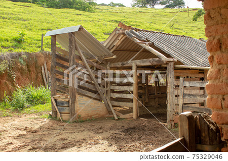 A kind of barn on a corral, after a heavy rain with the ground full of puddles. In the background there are a green pasture and blue sky 75329046