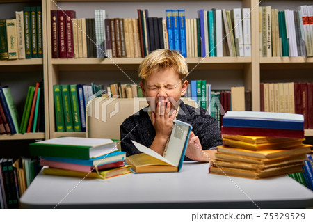 upset tired schoolboy yawning while studying 75329529