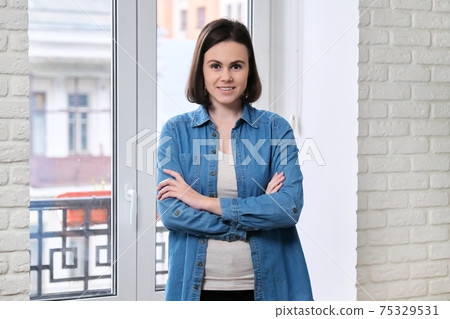 Portrait of young beautiful confident smiling woman in denim shirt with folded arms crossed Portrait of young beautiful confident smiling woman in denim shirt with folded arms crossed 75329531