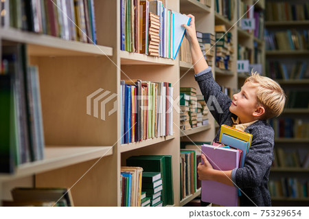 little school boy taking books from shelves in library, with a stack of books in hands little school boy taking books from shelves in library, with a stack of books in hands 75329654