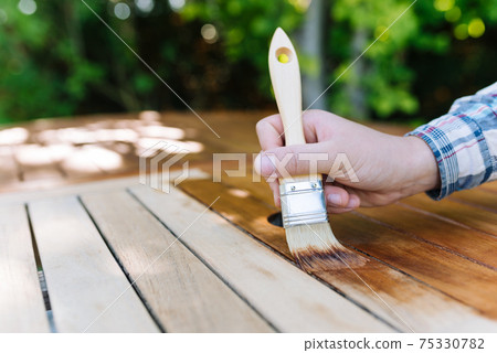 young woman painting wooden exotic wood table in the garden with a brush young woman painting wooden exotic wood table in the garden with a brush 75330782