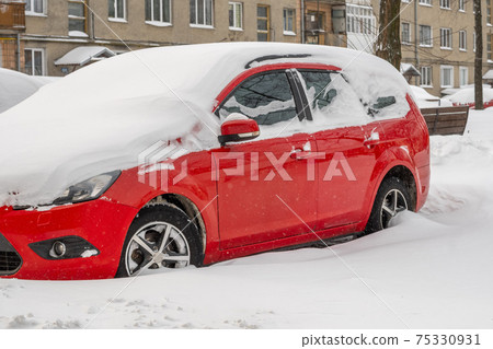 City street after blizzard. Stuck cars under the snow and ice. Buried vehicle in snowdrift on the road. Parking lots in winter after heavy snowfall. Uncleaned roads. Record-breaking amounts of snow. 75330931