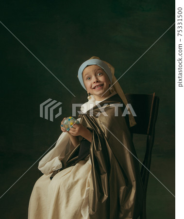 Medieval little girl as a lady with a pearl earring on dark studio background. Concept of comparison of eras, childhood. Stylish creative design, art vision, new look of artwork. 75331500