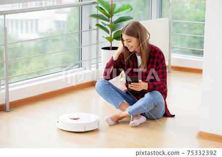 Young woman using automatic vacuum cleaner to clean the floor 75332392
