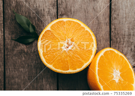 Sliced halves of orange fruit on gray wooden background. Pulp and green leaves Sliced halves of orange fruit on gray wooden background. Pulp and green leaves 75335269