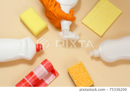 Sponges, garbage bags and a hand with bottles of washing and cleaning liquids on the beige background. Sponges, garbage bags and a hand with bottles of washing and cleaning liquids on the beige background. 75336200