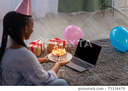 Black lady holding birthday cake in front of laptop screen Black lady holding birthday cake in front of laptop screen 75336479