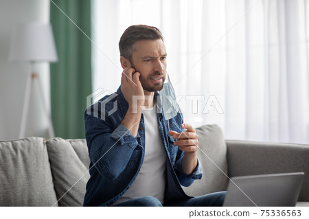 Bearded man removing face mask, scratching his beard Bearded man removing face mask, scratching his beard 75336563