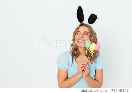 Portrait cheerful excited young woman wearing Easter bunny ears holding decorative colored eggs Portrait cheerful excited young woman wearing Easter bunny ears holding decorative colored eggs 75340342