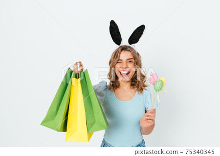 Easter shopping, cheerful young woman wearing bunny ears smiles Easter shopping, cheerful young woman wearing bunny ears smiles 75340345