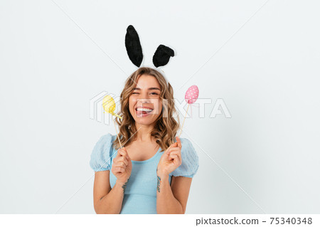 Cheerful young blonde woman wears Easter bunny ears holding decorative colored eggs Cheerful young blonde woman wears Easter bunny ears holding decorative colored eggs 75340348