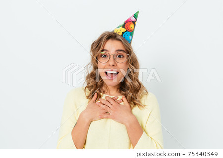 Happy amazed young woman wearing birthday cap smiling looking at camera Happy amazed young woman wearing birthday cap smiling looking at camera 75340349