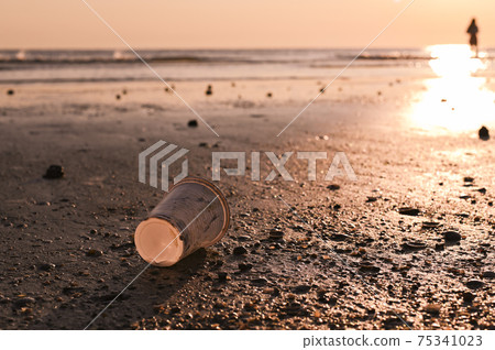 Plastic disposable cup on the beach in the sand. Ecological disaster and environmental pollution 75341023