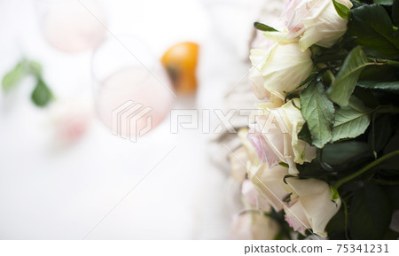Bouquet of white roses and wine. Close-up flowers and blurry wine glasses without focus. Free space Bouquet of white roses and wine. Close-up flowers and blurry wine glasses without focus. Free space 75341231