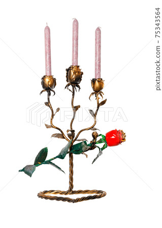 A metal forged candlestick in the form of rosebuds with three candles stands on a twisted stand with a red forged rose isolated on a white background. A metal forged candlestick in the form of rosebuds with three candles stands on a twisted stand with a red forged rose isolated on a white background. 75343564