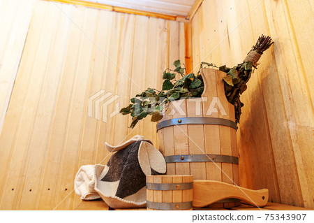 Interior details Finnish sauna steam room with traditional sauna accessories basin birch broom scoop felt hat towel. Traditional old Russian bathhouse SPA Concept. Relax country village bath concept. Interior details Finnish sauna steam room with traditional sauna accessories basin birch broom scoop felt hat towel. Traditional old Russian bathhouse SPA Concept. Relax country village bath concept. 75343907