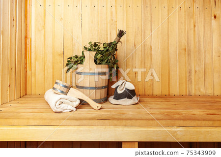 Interior details Finnish sauna steam room with traditional sauna accessories basin birch broom scoop felt hat towel. Traditional old Russian bathhouse SPA Concept. Relax country village bath concept. Interior details Finnish sauna steam room with traditional sauna accessories basin birch broom scoop felt hat towel. Traditional old Russian bathhouse SPA Concept. Relax country village bath concept. 75343909