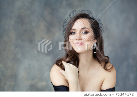 Elegant brunette model woman with long curly hair in black veil on gray stucco background Elegant brunette model woman with long curly hair in black veil on gray stucco background 75344178