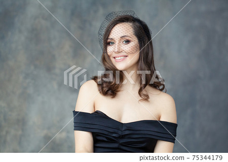Perfect woman in black veil smiling on gray background, portrait Perfect woman in black veil smiling on gray background, portrait 75344179
