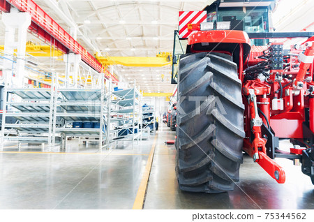 Blurred assembly workshop and tractor wheel at big industrial plant 75344562