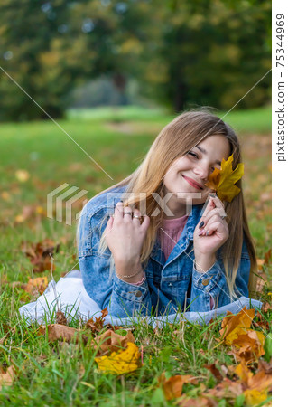A young girl lies on the grass in a warm autumn in the evening with a petal in her hands. 75344969