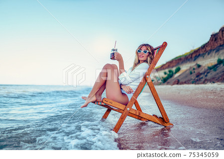 Pretty woman relaxing on a lounger beach and drinks soda water. Pretty woman relaxing on a lounger beach and drinks soda water. 75345059