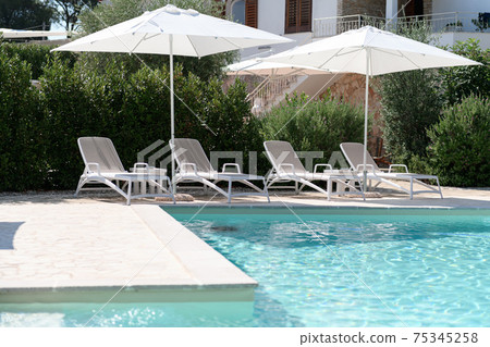 Swim pool with clear blue water and sun beds on sunny day in a yard Swim pool with clear blue water and sun beds on sunny day in a yard 75345258