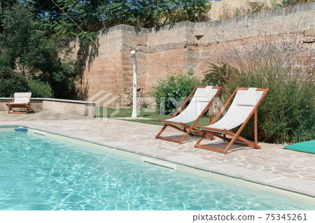 Swim pool with clear blue water and two sun bed on sunny day in a yard Swim pool with clear blue water and two sun bed on sunny day in a yard 75345261