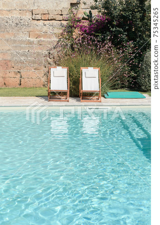 Swim pool with clear blue water and sun beds on sunny day 75345265