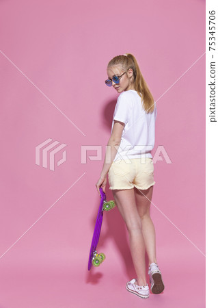 Cheerful young girl with a skateboard on the pink background 75345706