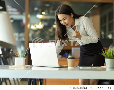 Female entrepreneur celebrating on her accomplishment while standing in workplace 75349433