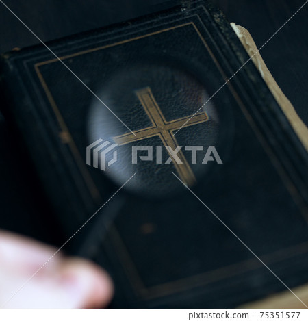 Vintage antique bible book on table and magnifying glass in human hand. Vintage antique bible book on table and magnifying glass in human hand. 75351577