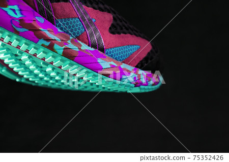 A sporty running shoe with a textured green sole on a black background. A sporty running shoe with a textured green sole on a black background. 75352426