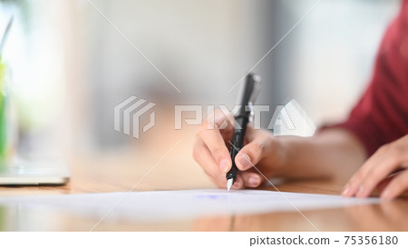 Closeup female signing document focus on her hand holding pen putting signature on official paper. Closeup female signing document focus on her hand holding pen putting signature on official paper. 75356180