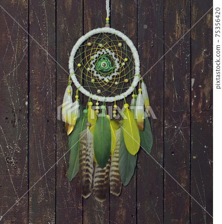 Beautiful handmade boho dreamcatcher with green, yellow and white feathers and medalion. Mystic background with dream catcher against wooden planks, esoteric, ethnic and spiritual concept Beautiful handmade boho dreamcatcher with green, yellow and white feathers and medalion. Mystic background with dream catcher against wooden planks, esoteric, ethnic and spiritual concept 75356420