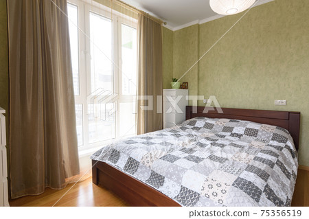 Bedroom interior with a large double bed and a large stained glass window with tulle and curtains Bedroom interior with a large double bed and a large stained glass window with tulle and curtains 75356519
