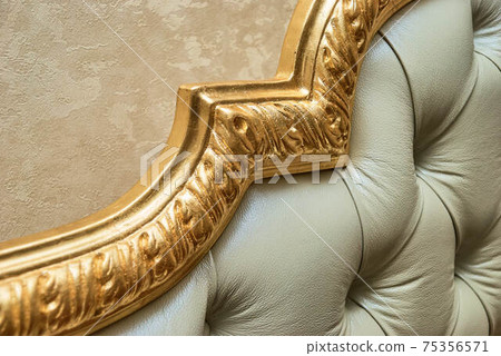 Headboard of beige leather and carved golden molding closeup 75356571