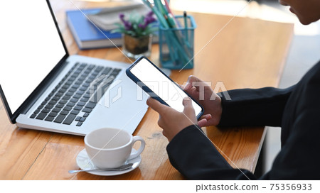 Cropped shot of young businesswoman using smart phone while sitting in front of computer laptop at office. Cropped shot of young businesswoman using smart phone while sitting in front of computer laptop at office. 75356933