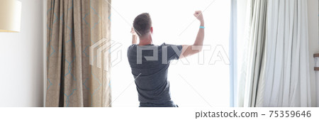 Man stands with his back against window and holds his hands up 75359646
