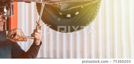 An auto mechanic removes the undershield of an internal combustion engine on a car. Scheduled maintenance and oil change of the machine An auto mechanic removes the undershield of an internal combustion engine on a car. Scheduled maintenance and oil change of the machine 75360203